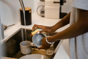 Close-up of woman washing dishes at kitchen sink, highlighting hands with bracelet.